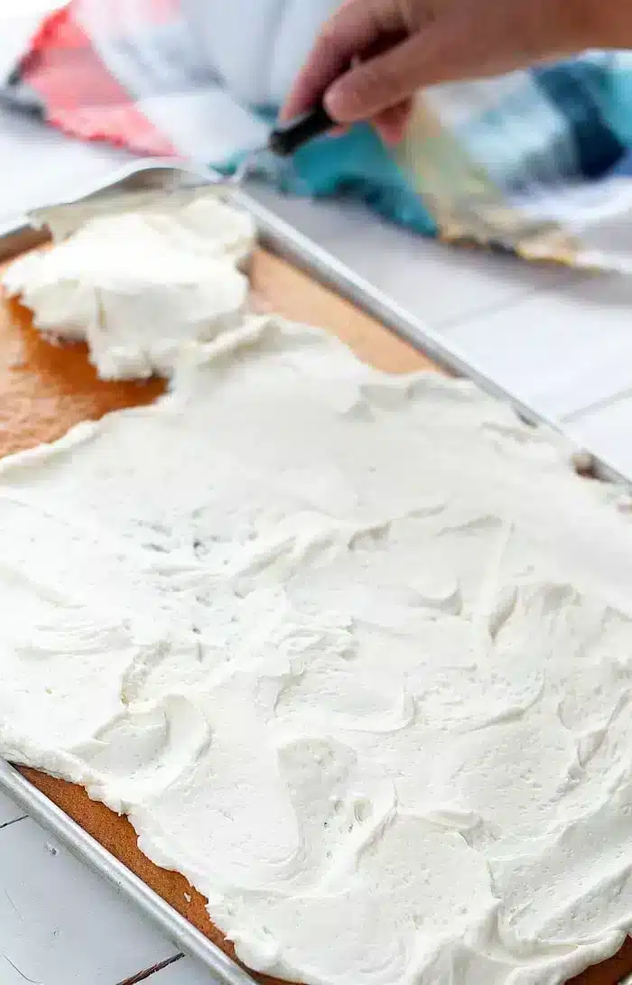 A tray of 1/2 sheet cake is being frosted with white icing. 