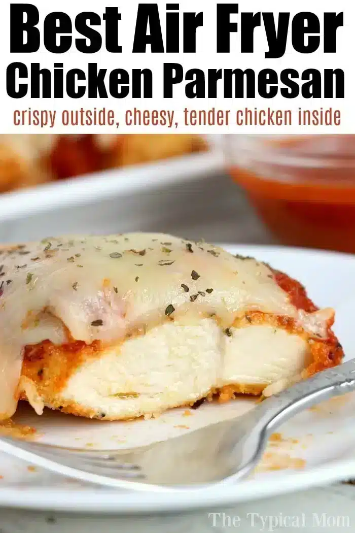 Close-up of a slice of air fryer chicken parm on a white plate, topped with melted cheese and herbs. The background shows a blurred dish and a small bowl of sauce. Text at the top reads, "Best Air Fryer Chicken Parmesan, crispy outside, cheesy, tender chicken inside.