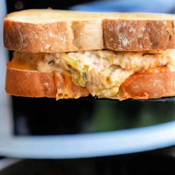 A close-up of a toasted sandwich reveals its creamy filling featuring artichokes, reminiscent of an air fryer tuna melt. The bread is golden brown, with the delicious filling peeking from the bitten corner.