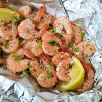 Grilling frozen shrimp seasoned with herbs and spices, garnished with lemon wedges, served elegantly on aluminum foil.