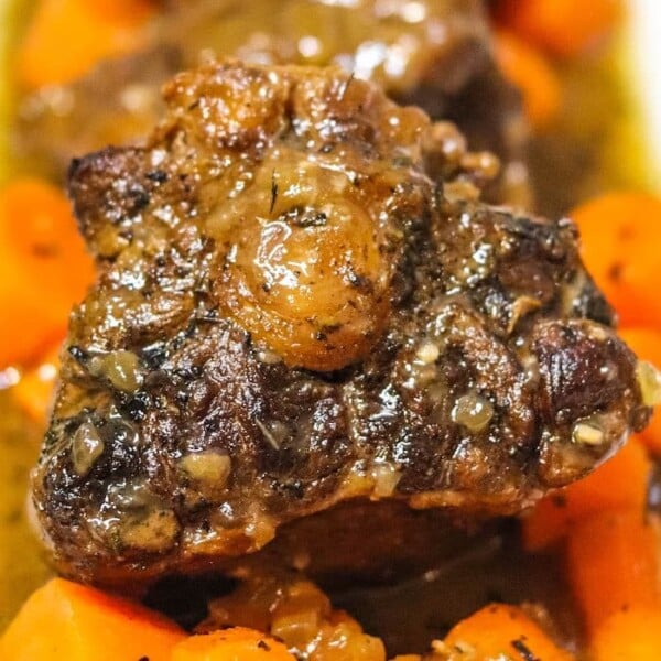 Close-up of a plate featuring braised oxtails on the stove, covered in a rich sauce and surrounded by chopped carrots. The beef is well-cooked, with a slightly charred exterior, and the carrots appear tender and flavorful.