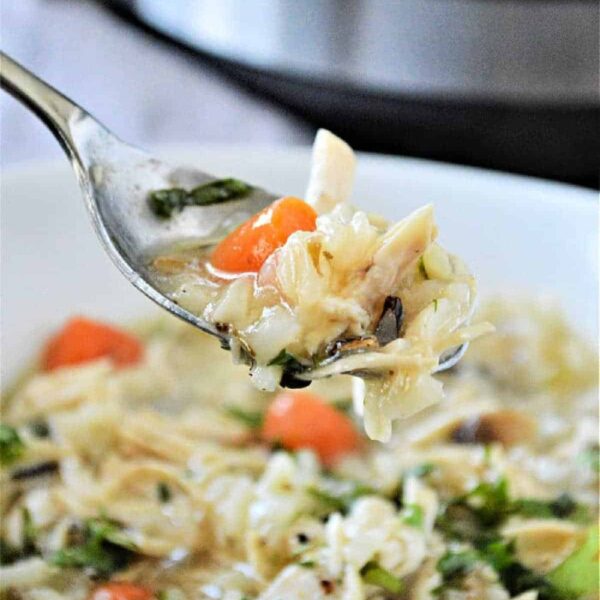 Spoon with chicken cabbage soup, carrots, and herbs held over a bowl, with an Instant Pot cooker in the background, perfect for making chicken rice soup.