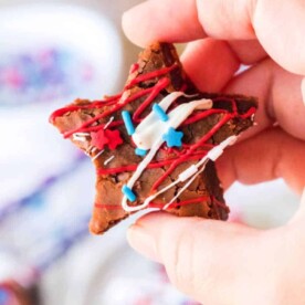 A hand holds a star-shaped, Two Bite Brownie from scratch, adorned with red, white, and blue icing and sprinkles.