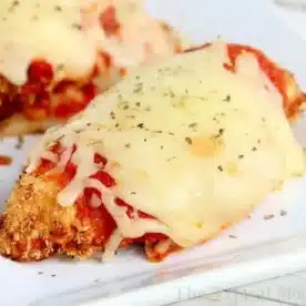 Close-up of air fryer chicken parm topped with melted cheese and tomato sauce, garnished with herbs, served on a white plate.