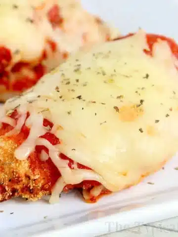 Close-up of air fryer chicken parm topped with melted cheese and tomato sauce, garnished with herbs, served on a white plate.