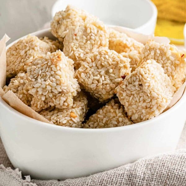 A white bowl filled with sesame-covered tofu nuggets rests on a cloth napkin.