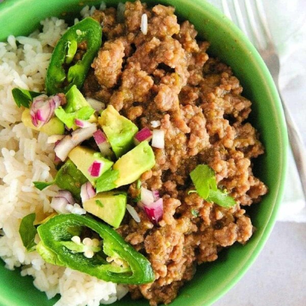 A green bowl with rice, slow cooker taco meat, avocado chunks, jalapeño slices, and diced red onion.