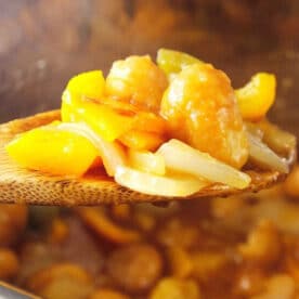 A wooden spoon holds instant pot sweet and sour chicken with bell peppers and onion over a pot.