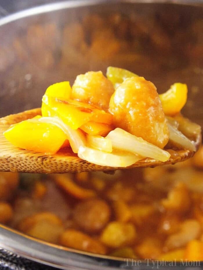 A wooden spoon holds instant pot sweet and sour chicken with bell peppers and onion over a pot.