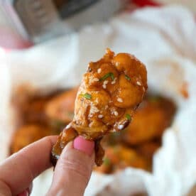 A hand holds a saucy chicken wing, topped with sesame seeds and herbs—perfect inspiration for making juicy pressure cooker frozen chicken wings at home.