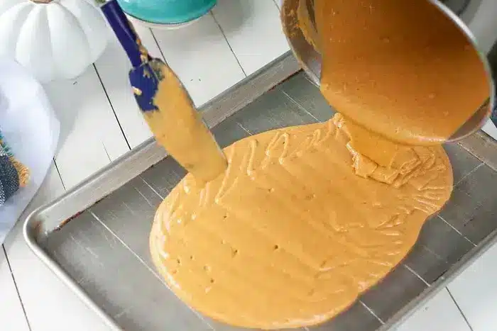 A thick, caramel-colored mixture is being poured from a pot onto a large metal baking sheet, perfect for creating a delightful 1/2 sheet cake. 