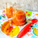 Two jars of delicious orange baby food rest on a colorful towel with a red spoon, freshly crafted using an Instant Pot for optimal flavor and nutrition.