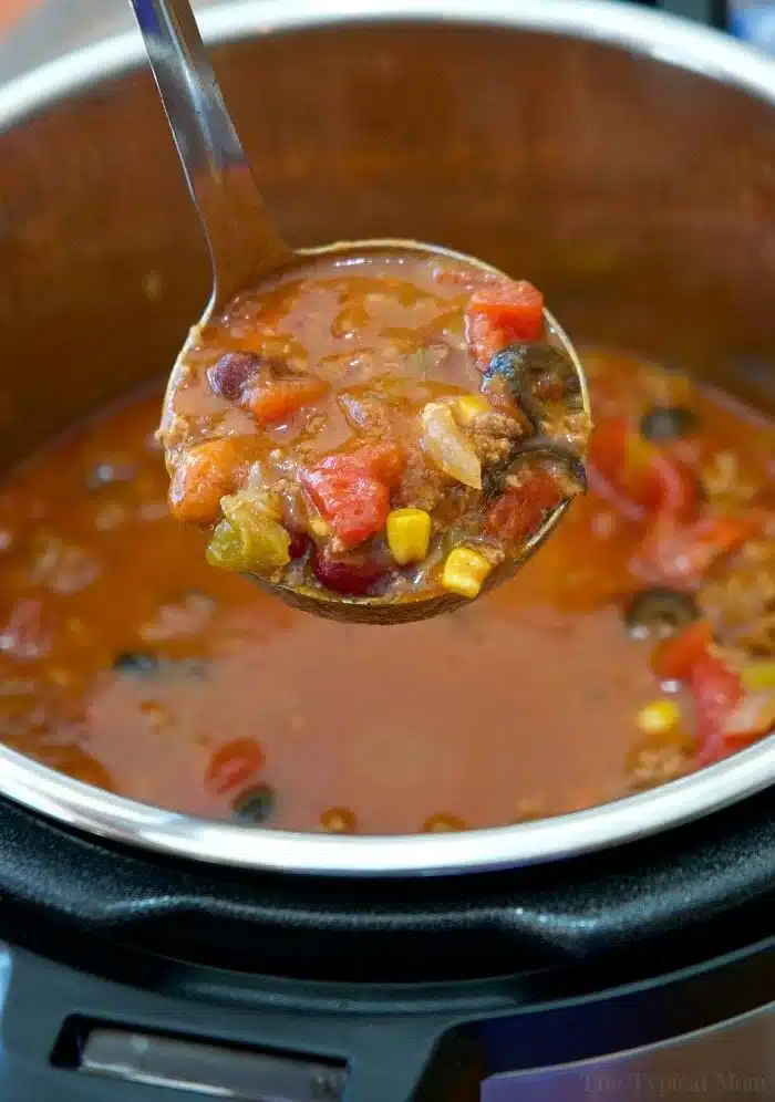 A ladle filled with hearty stew, crafted from leftover taco meat, hovers above a pot. The stew combines tomatoes, corn, and black beans in a rich broth. This delicious creation simmers perfectly within an electric pressure cooker.