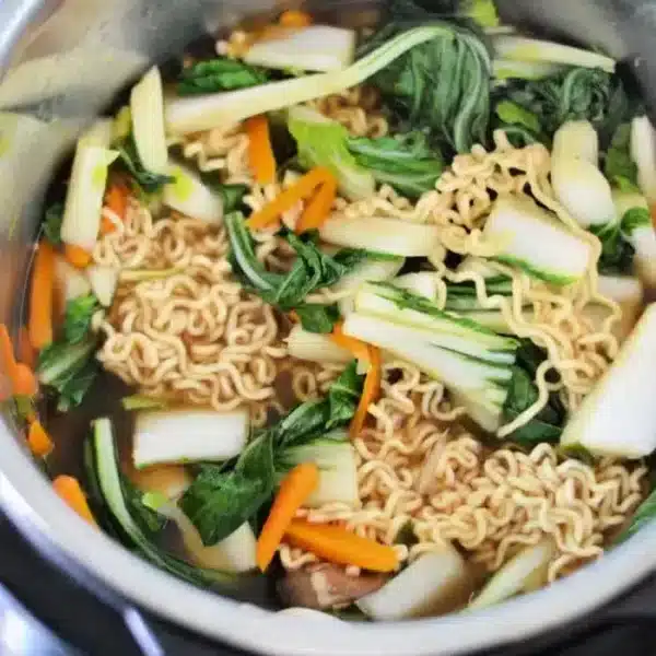 A pot filled with Instant Pot Vegetable Ramen features cooked instant noodles, chopped bok choy, carrot slices, and zucchini pieces in flavorful broth.