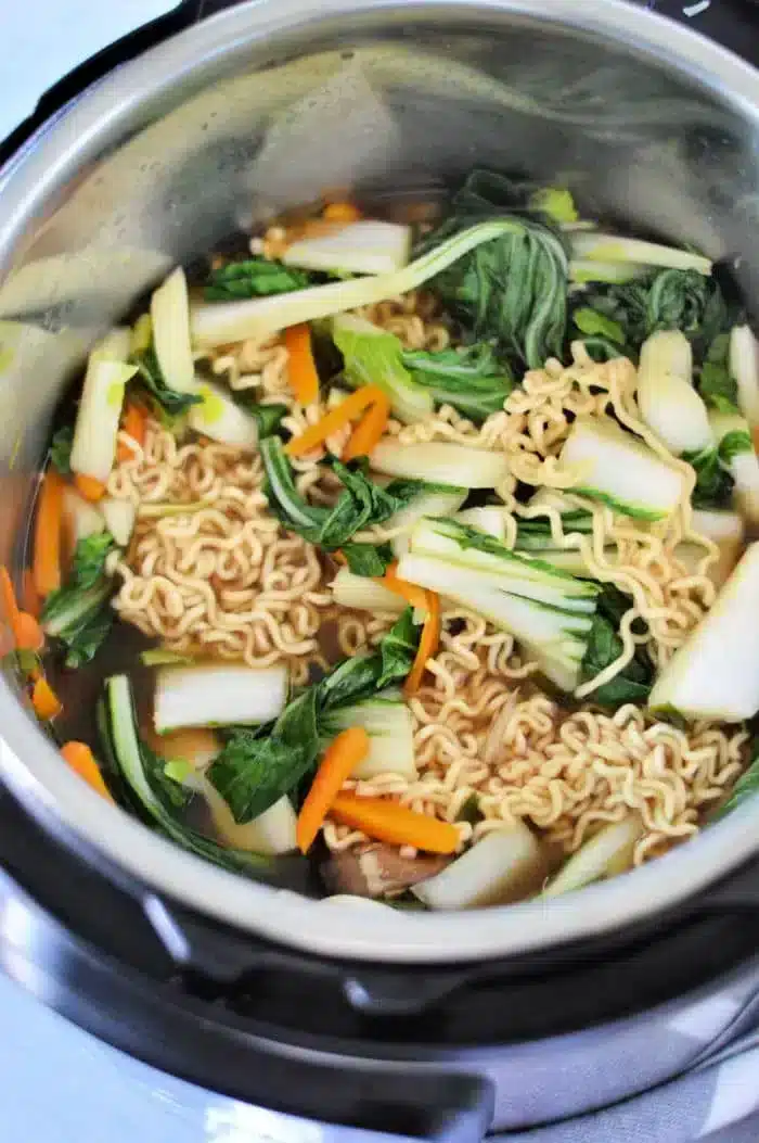 A pot filled with Instant Pot Vegetable Ramen features cooked instant noodles, chopped bok choy, carrot slices, and zucchini pieces in flavorful broth.