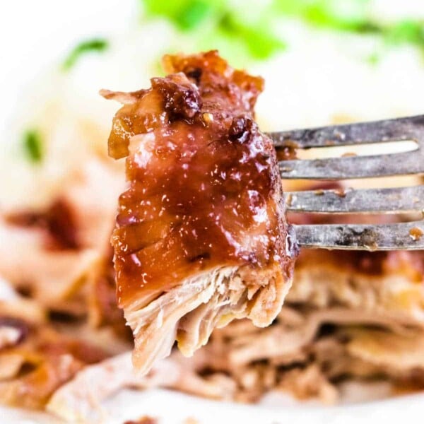 A fork holds a succulent piece of juicy, glazed pulled pork, with fresh greens blurred in the background—reminiscent of the mouthwatering tenderness found in slow-cooked BBQ chicken thighs.