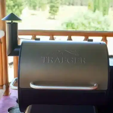 A Traeger grill stands proudly on a wooden deck, set against a forested landscape, perfect for exploring easy smoker recipes amidst nature's beauty.