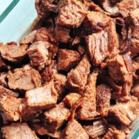 A clear glass dish filled with cubed, air fryer-cooked brisket reveals a browned exterior and tender interior. The meat is arranged in a slightly disorganized pile, with some pieces boasting a crispy texture.