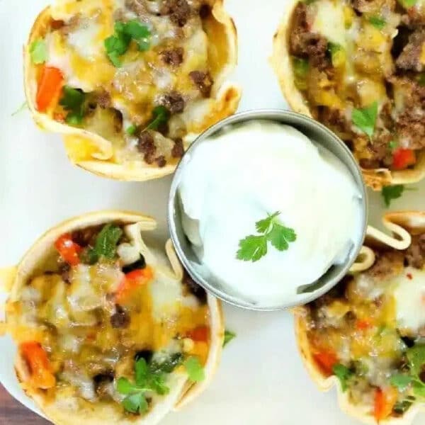 Steak fajita cups with ground beef, cheese, and veggies, served with a side of sour cream and garnished with fresh cilantro.