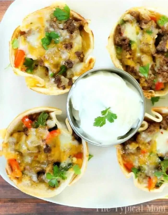 Steak fajita cups with ground beef, cheese, and veggies, served with a side of sour cream and garnished with fresh cilantro.