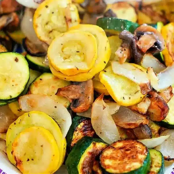 A dish featuring air fryer vegetables, including sautéed yellow squash, zucchini, mushrooms, and onions. The sliced veggies are seasoned to perfection with a delightful browning from cooking. This colorful mixture is beautifully presented on a plate.