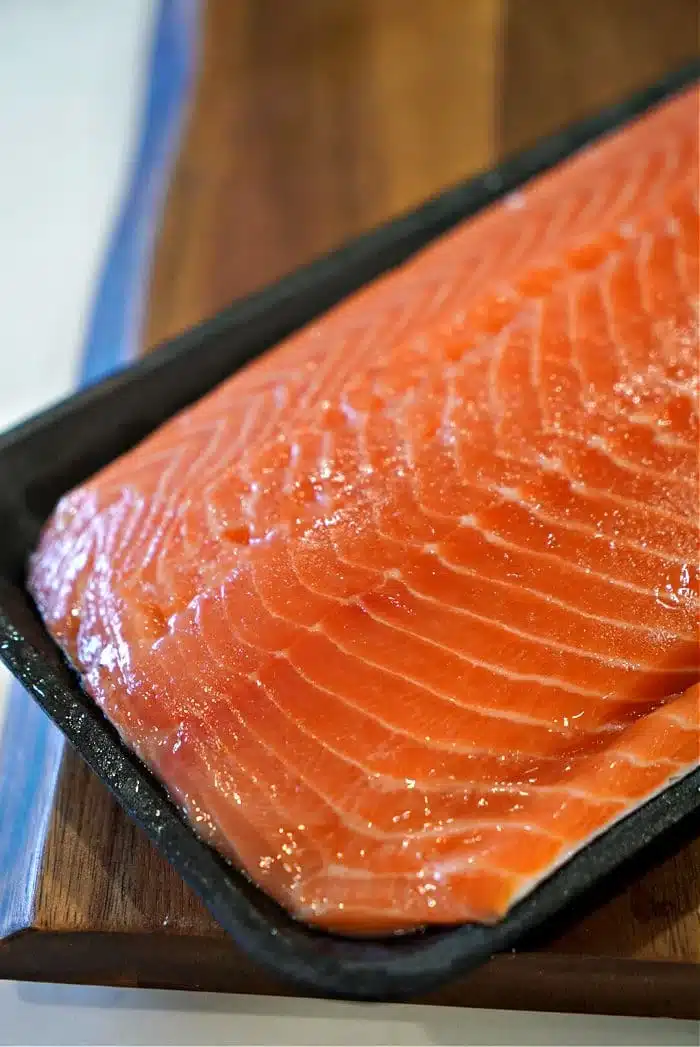 A close-up view of a raw salmon fillet on a dark rectangular tray captures the vibrant orange color and visible marbling, perfect for making oven-baked teriyaki salmon in foil. The tray rests elegantly on a wooden surface, ready for its culinary transformation.