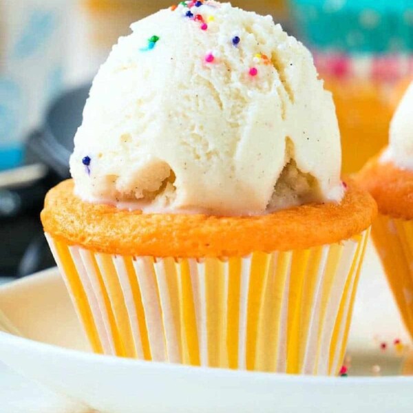 A delightful vanilla cupcake, created using a soda cake mix, topped with a scoop of ice cream and colorful sprinkles on a pristine white plate.