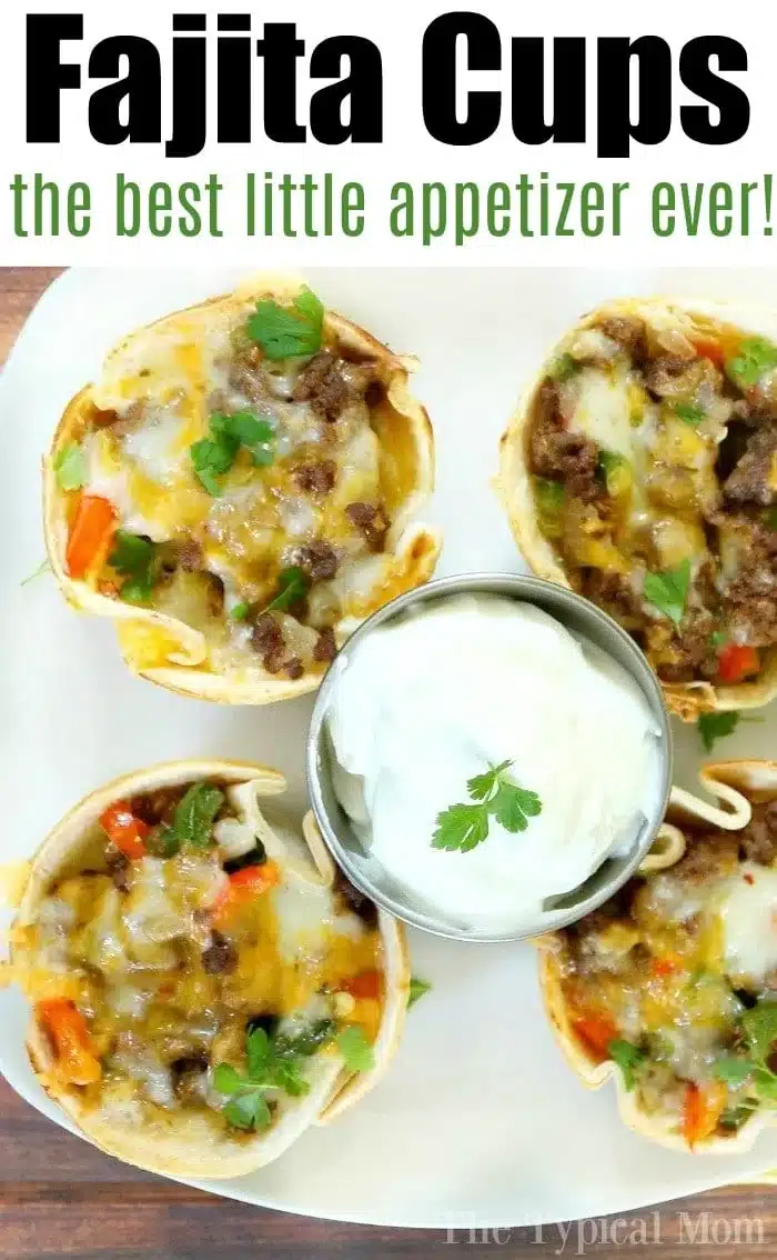 Four steak fajita cups overflowing with ground meat, melted cheese, and vegetables are artfully arranged on a plate. In the center, a small dish of sour cream garnished with a cilantro leaf waits to be savored. Above reads: Fajita Cups, the best little appetizer ever!