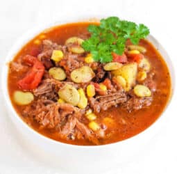 A bowl of crockpot Brunswick stew with tender meat, corn, and lima beans, all garnished with a sprinkle of fresh parsley.