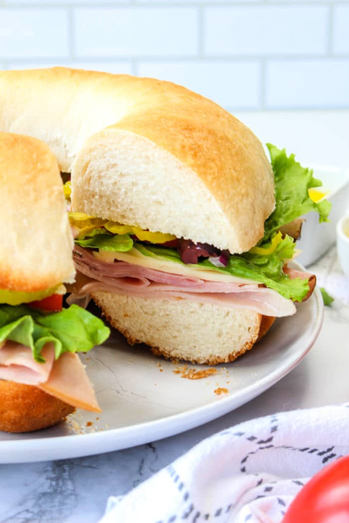 A sliced bundtwich sandwich with ham, lettuce, and vegetables on a white plate resembles an artisanal take on how to make a bundtwich.