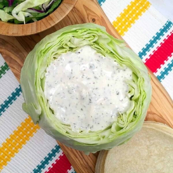 Cabbage salad with creamy cilantro lime dressing sits on a wooden board with a colorful cloth underneath, bringing a fresh, zesty twist reminiscent of sauce for fish tacos.