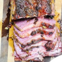 Sliced beef roast, reminiscent of air fryer corned beef, boasts a charred exterior on a wooden cutting board. The inside is pink with a glazed, crispy surface, and juices glisten on the board.