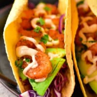 Close-up of two shrimp tacos with avocado slices, red cabbage, and creamy sauce in corn tortillas. Discover how to make shrimp tacos with frozen cooked shrimp for a quick and delightful meal option.