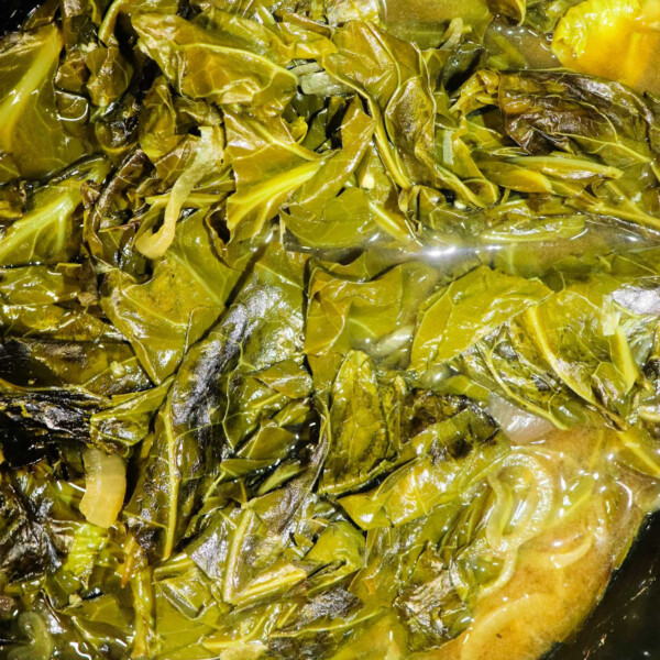 Close-up of slow cooker collard greens in broth, showing wilted leaves and a rich, dark liquid.