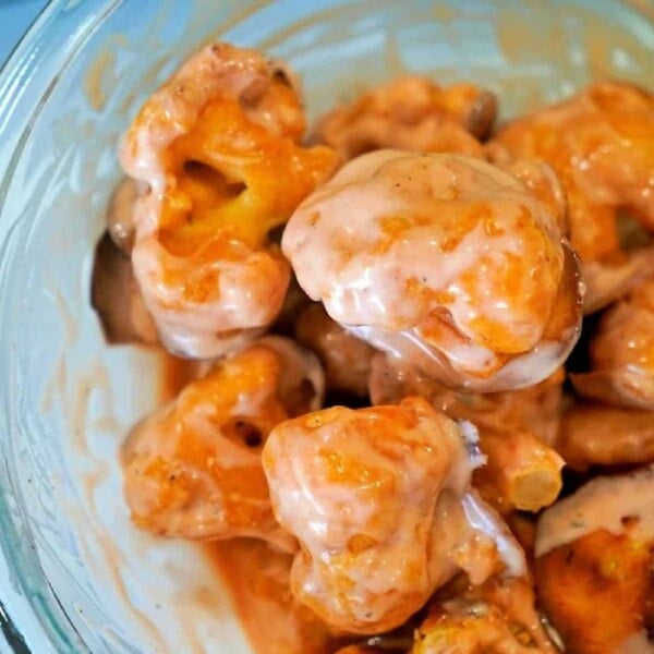 A glass bowl brimming with buffalo-baked cauliflower florets, each perfectly coated in vibrant orange buffalo sauce.