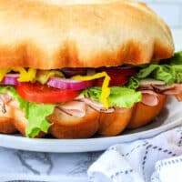 Learn how to make a bundtwich: a large sandwich with turkey, lettuce, tomato, red onion, and peppers, all perfectly nestled on a round bun. Serve it beautifully presented on a plate for the ultimate feast.