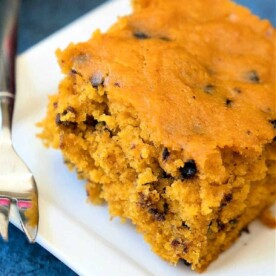 A slice of crockpot pumpkin bread cake with chocolate chips rests invitingly on a white plate.