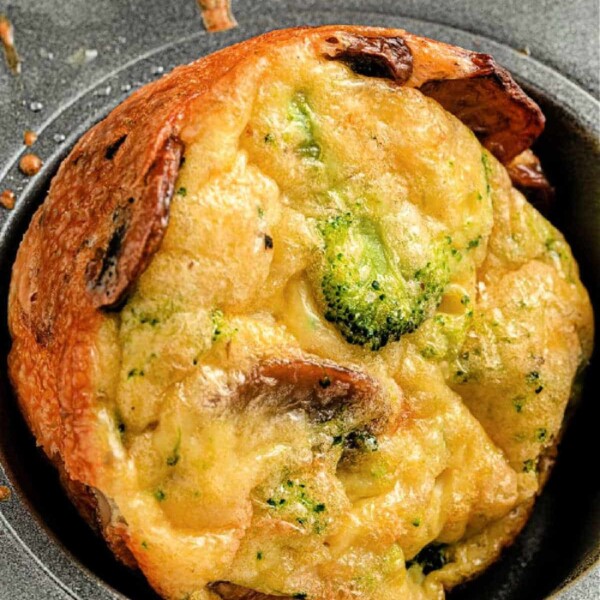 Close-up of a crustless broccoli quiche muffin with mushroom pieces nestled in a muffin tin.