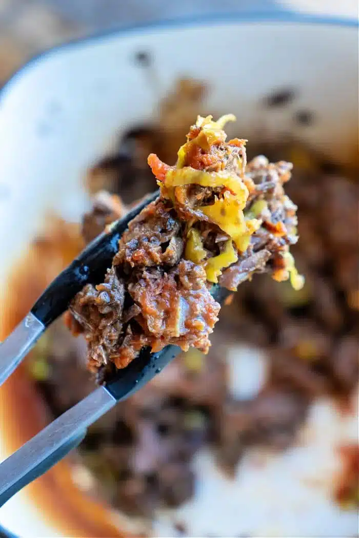 Close-up of a fork holding a piece of cooked shredded beef from frozen, mixed with melted cheese and diced vegetables, with more of the savory dish blurred in the background.