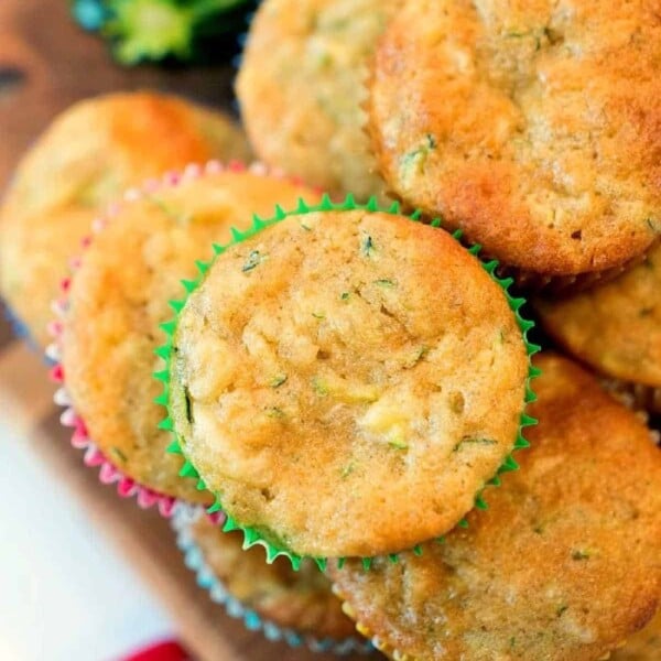 A stack of banana zucchini muffins in colorful liners sits invitingly on a wooden surface.