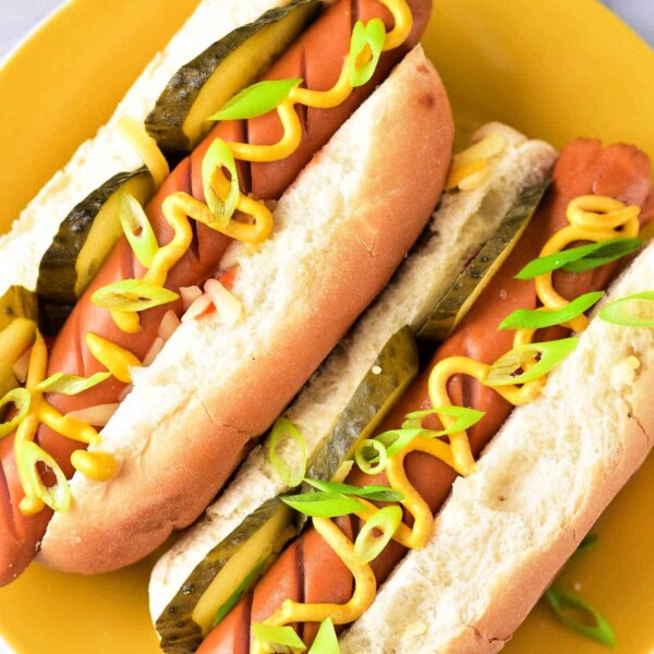 Two perfectly cooked hot dogs, fresh from the microwave, are topped with mustard, pickles, and green onions on a vibrant yellow plate.