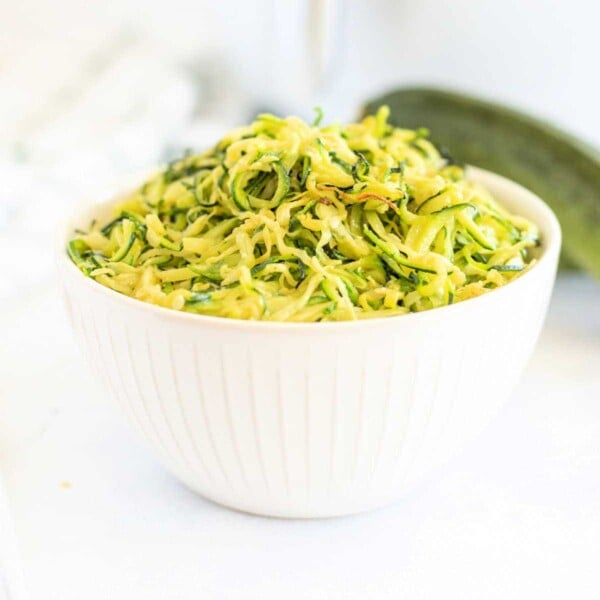 A white bowl filled with zucchini noodles on a light background showcases a delicious twist on traditional dishes, perfect for your next zucchini dinner recipe.