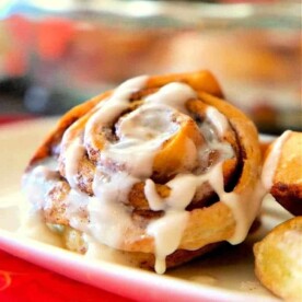 A plate features Bisquick Cinnamon Rolls drizzled with white icing, alongside crispy potato wedges.