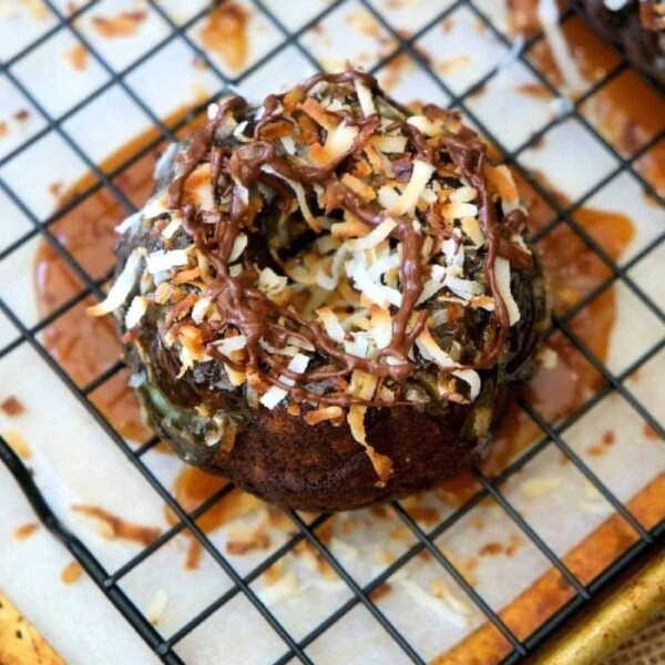 Chocolate donut topped with toasted coconut and drizzled caramel cools on a rack, tempting you to wonder how long it takes to bake such sweet mini bundt cake delights.