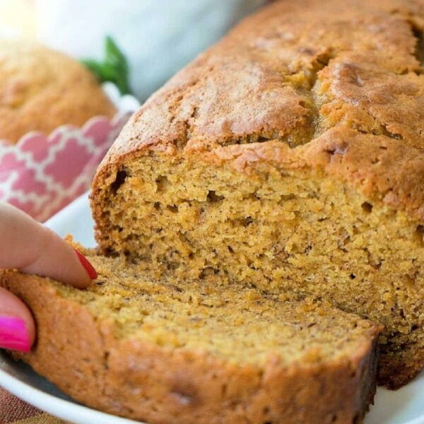 A person slices into a loaf of moist, golden-brown pumpkin banana bread on a white plate.