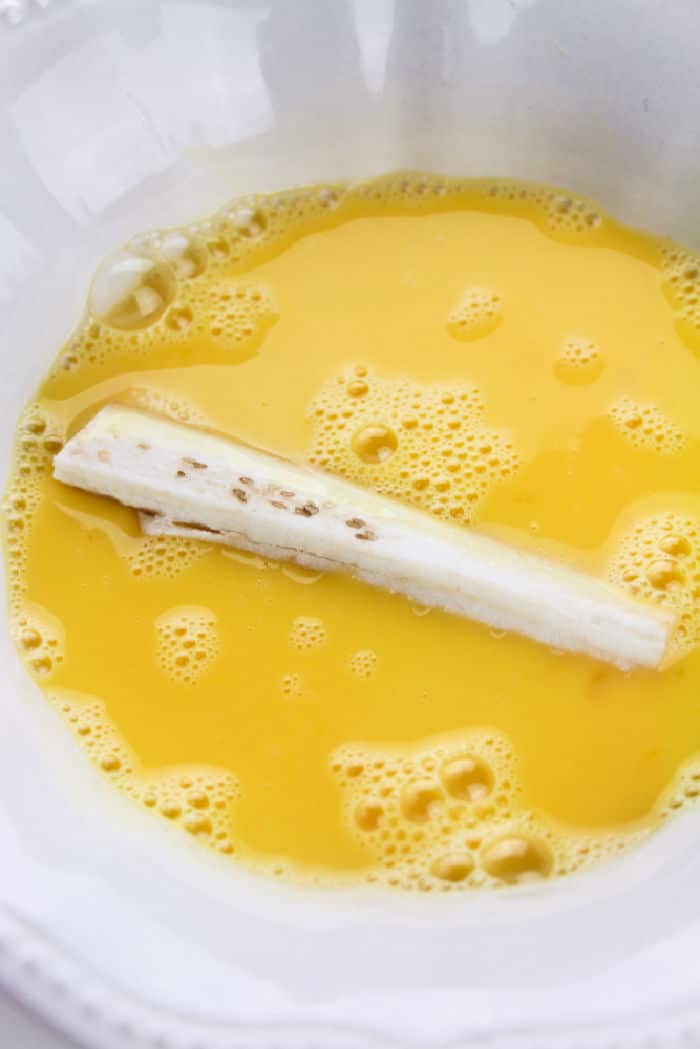 Egg mixture in a white bowl with a eggplant stick floating on top, reminiscent of the comforting aroma that accompanies freshly baked eggplant fries.