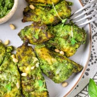 Air Fryer Pesto Chicken pieces are perfectly grilled and coated in green pesto sauce, served on a plate garnished with fresh greens and pine nuts.