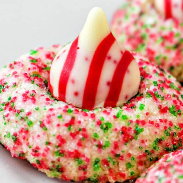 A close-up of a Hershey Kiss Christmas cookie topped with a striped chocolate, coated in red and green sugar sprinkles for a festive touch.