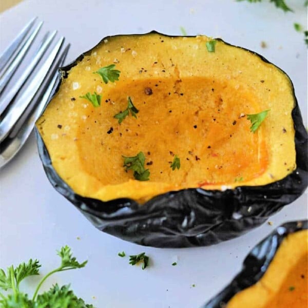 microwave acorn squash halves, perfectly seasoned with pepper and garnished with parsley, rest invitingly on a white surface next to a fork—a delightful dish you can easily prepare by learning how to cook acorn squash in the microwave.