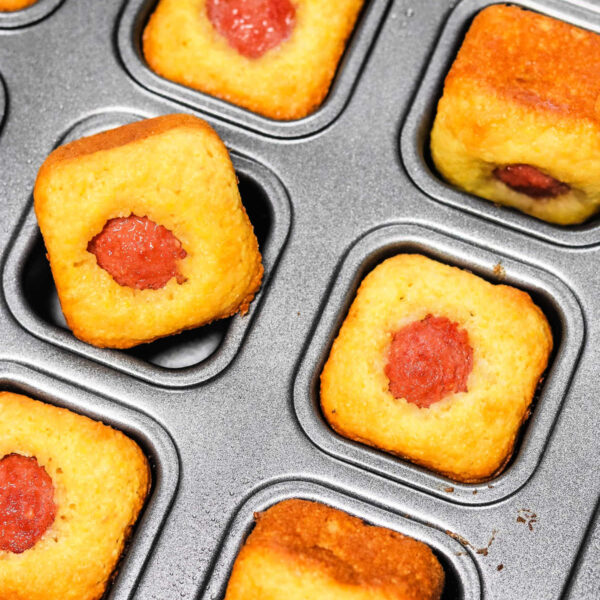 Mini corn dog bites nestled in a baking tray, each featuring a small hot dog piece at their center.